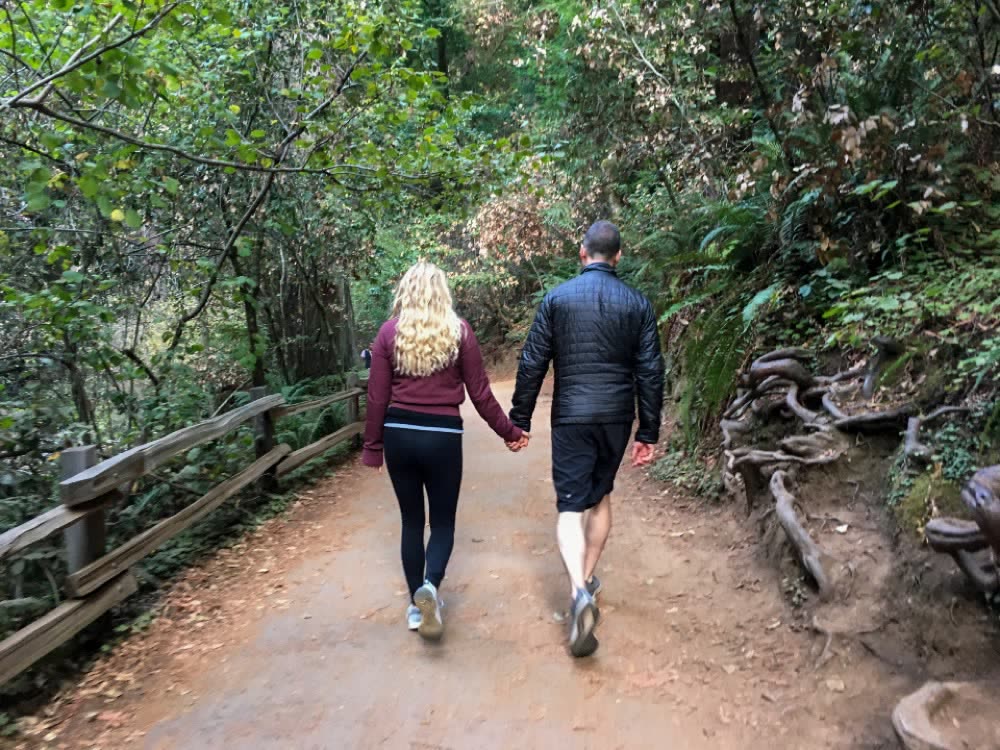 Couple walking hand in hand along a shady wooded trail